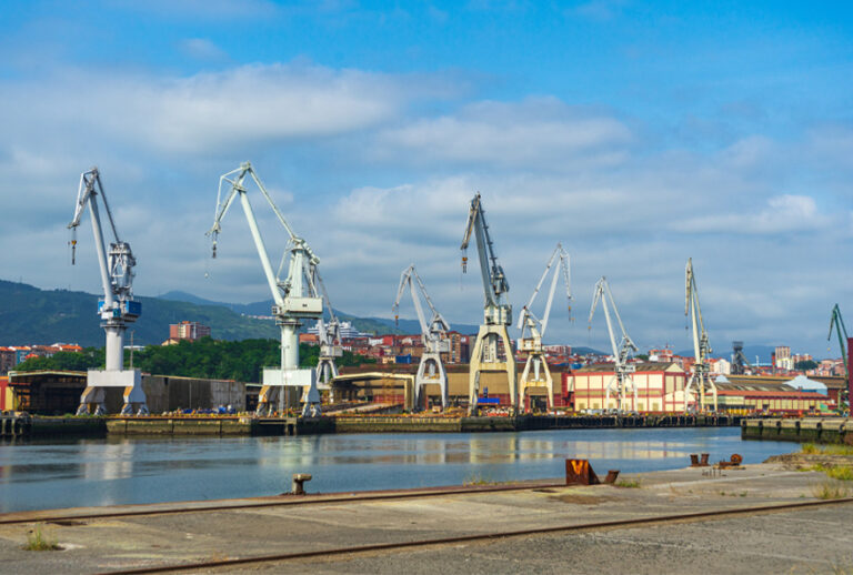 A imagem mostra um porto industrial com guindastes e edifícios ao fundo, ilustrando o impacto do aumento do imposto de importação.